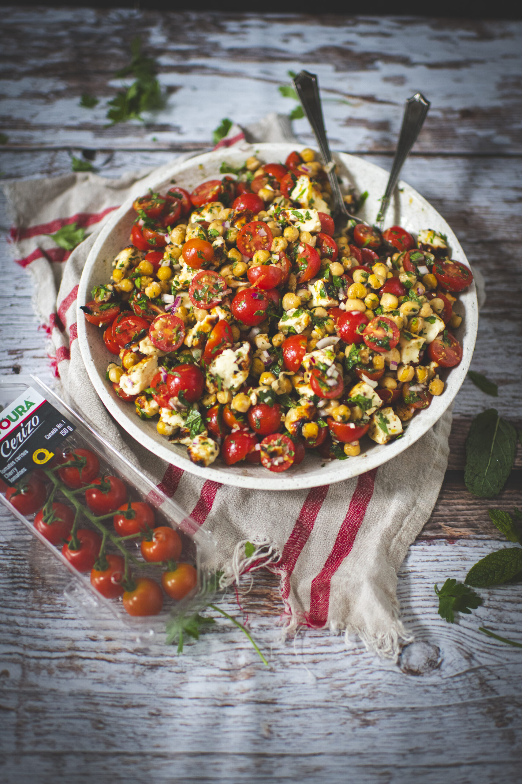 Salade de tomates cerises, pois chiches, halloumi sur une table en bois rustique avec un emballage de tomates CERIZO de SAVOURA