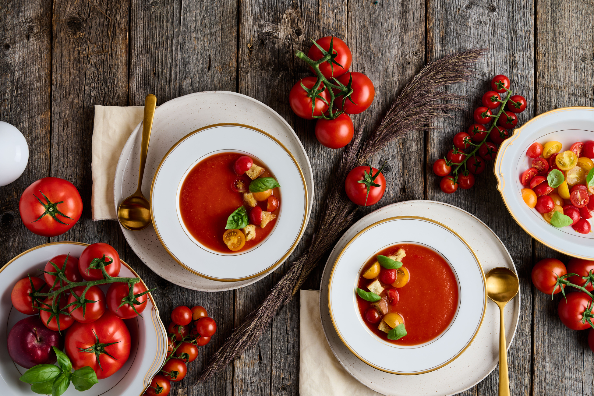 Mise en scène d'une table automnale avec des bols remplis de potage aux tomates et aux pommes et comme décoration les ingrédients qui entourent les bols.